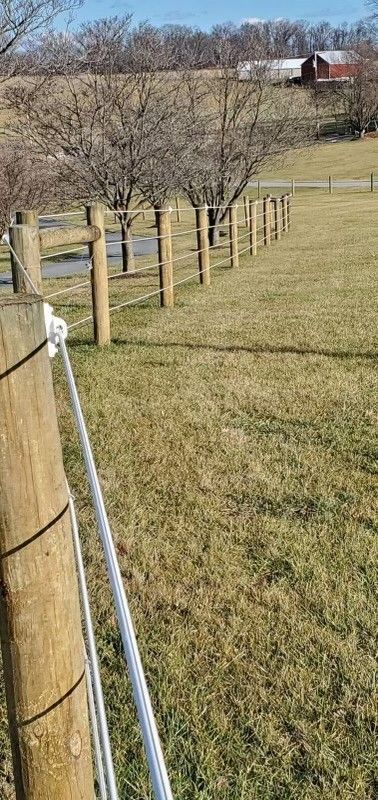 A wooden fence surrounds a grassy field with a barn in the background.