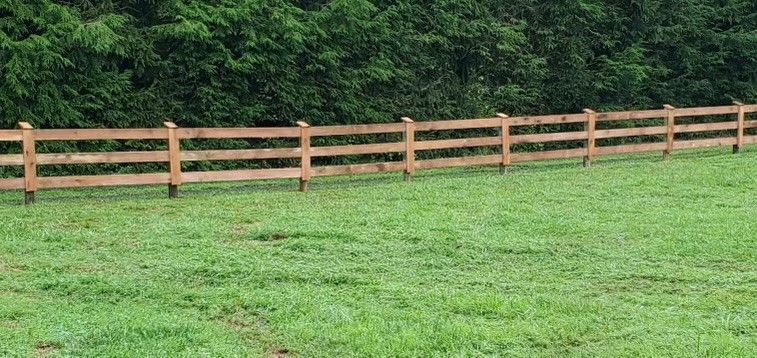 A wooden fence surrounds a lush green field.