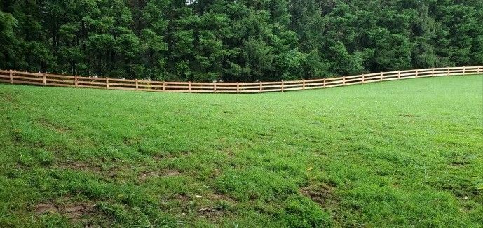 A wooden fence surrounds a lush green field.