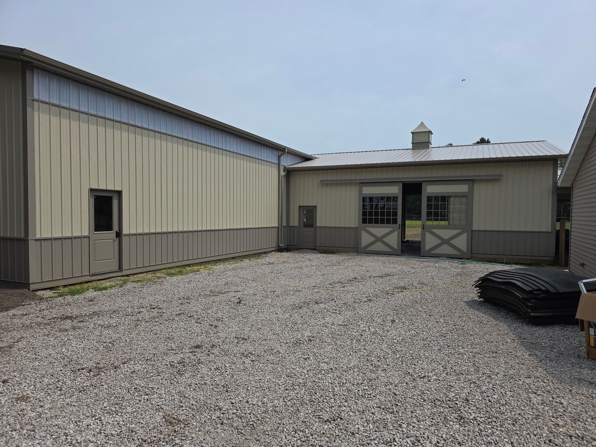 Gravel yard with two light-colored metal buildings, one with sliding doors. Gray sky.