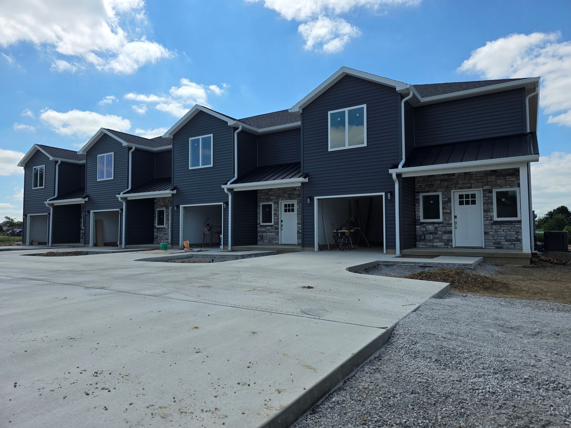 Row of newly constructed townhouses with dark blue siding, stone accents, and open carports.
