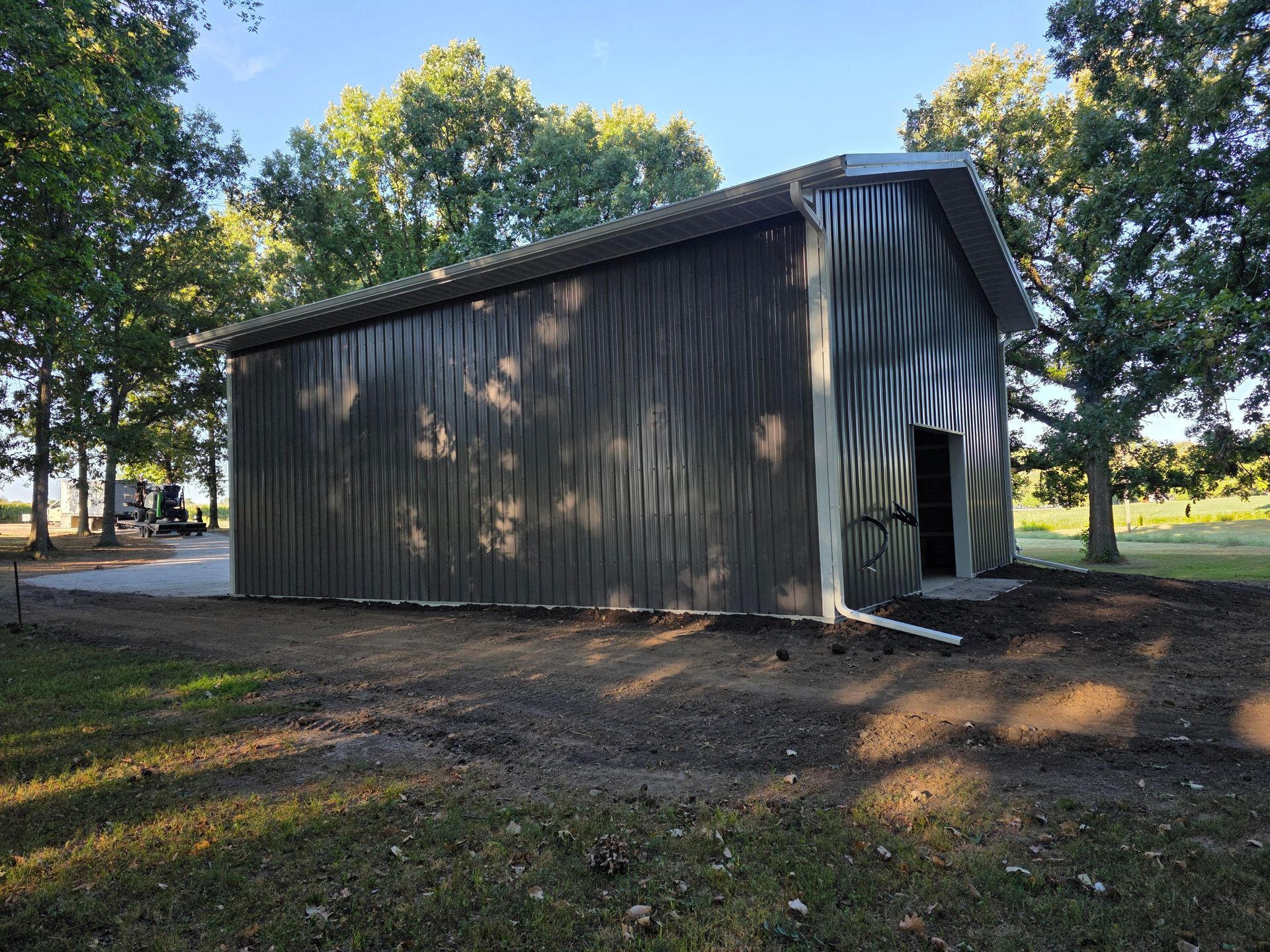 Metal shed with a dark exterior, open door, and trees in the background.