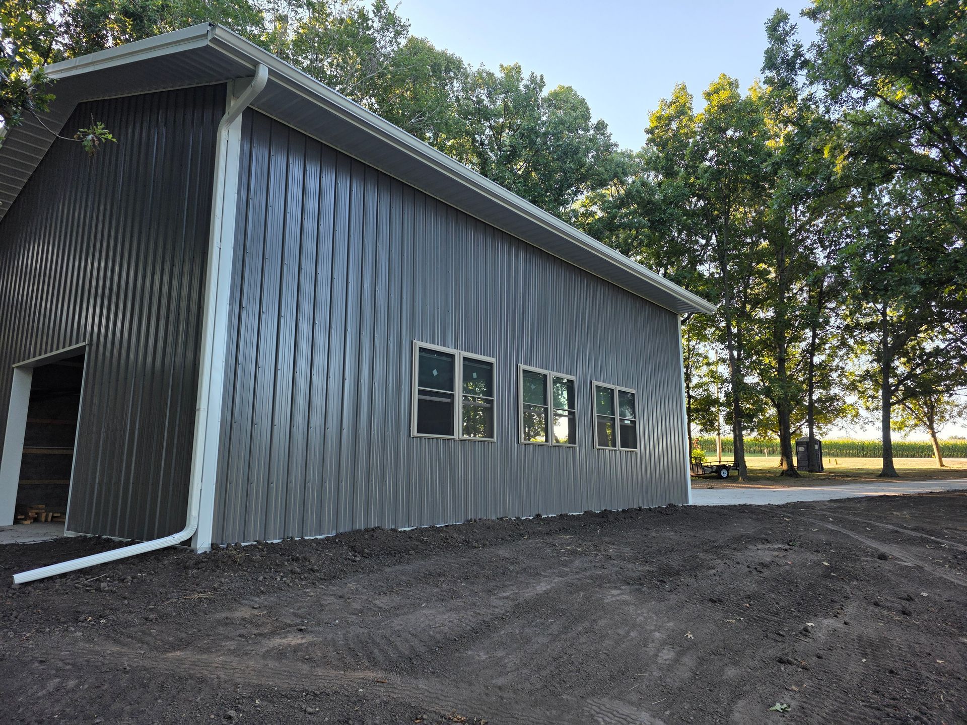 Gray metal building with multiple windows, set in a yard, trees in the background, and a driveway.