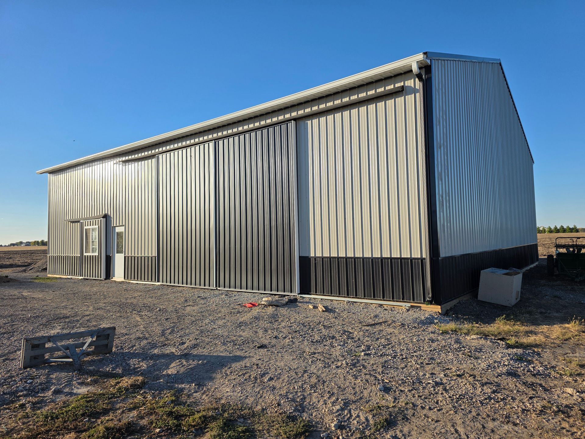 Metal barn with large sliding doors on gravel, under a blue sky.