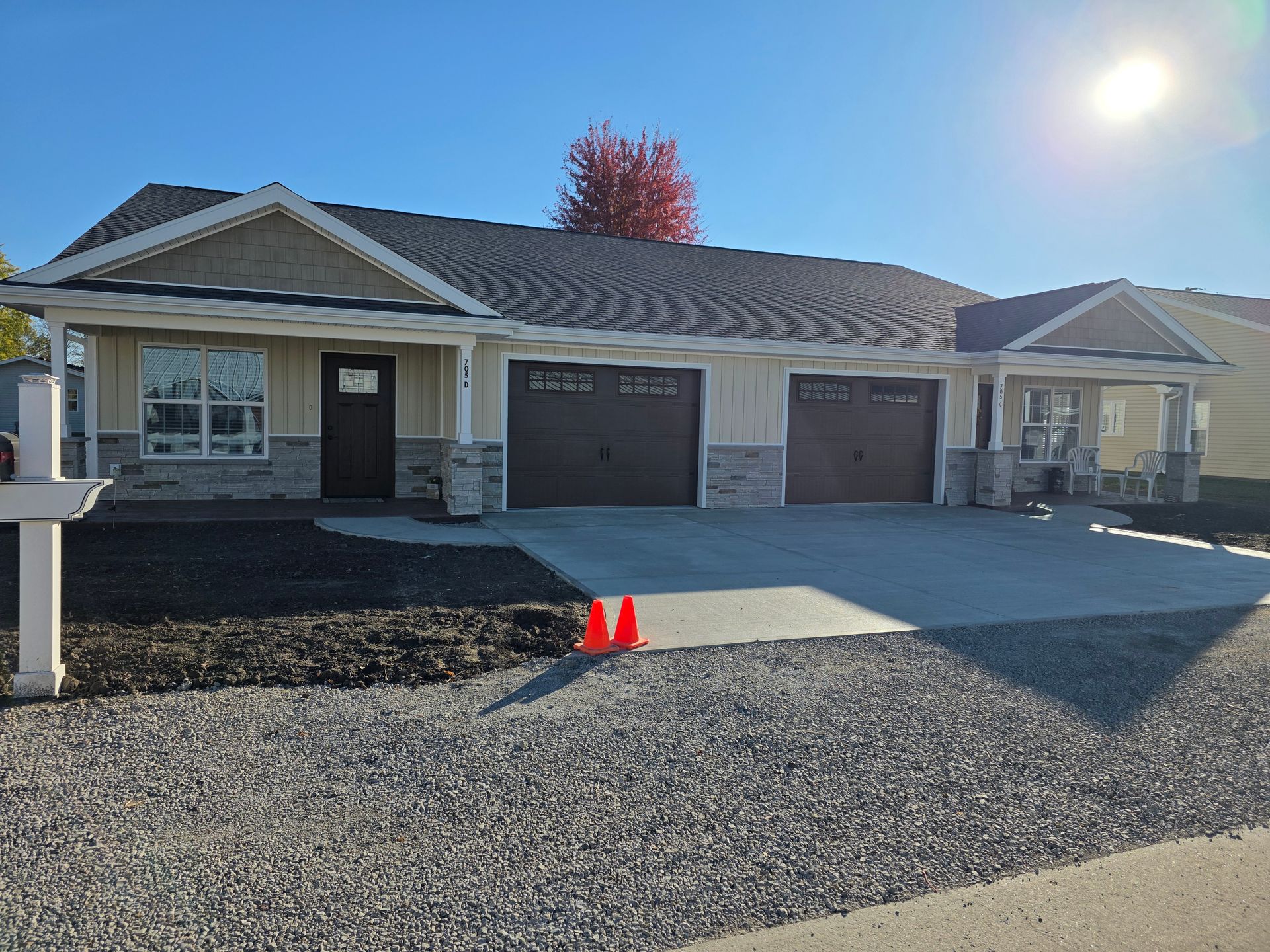 Tan and grey ranch-style house with three-car garage, concrete driveway, and black mulch.