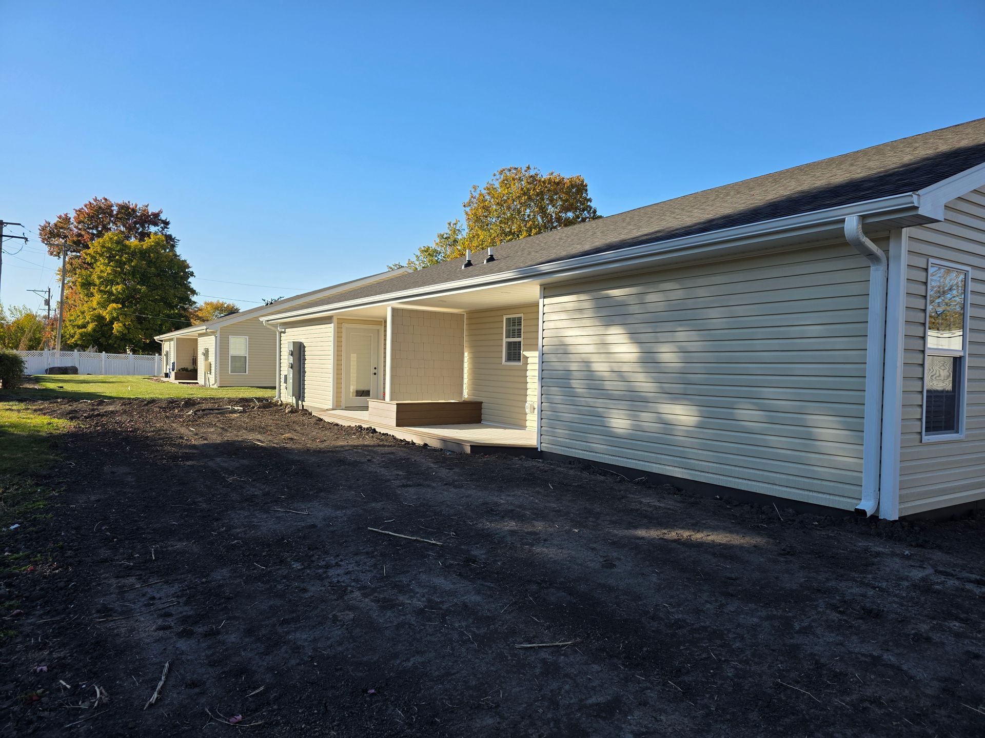 Row of newly constructed tan siding homes with covered patios against a blue sky.