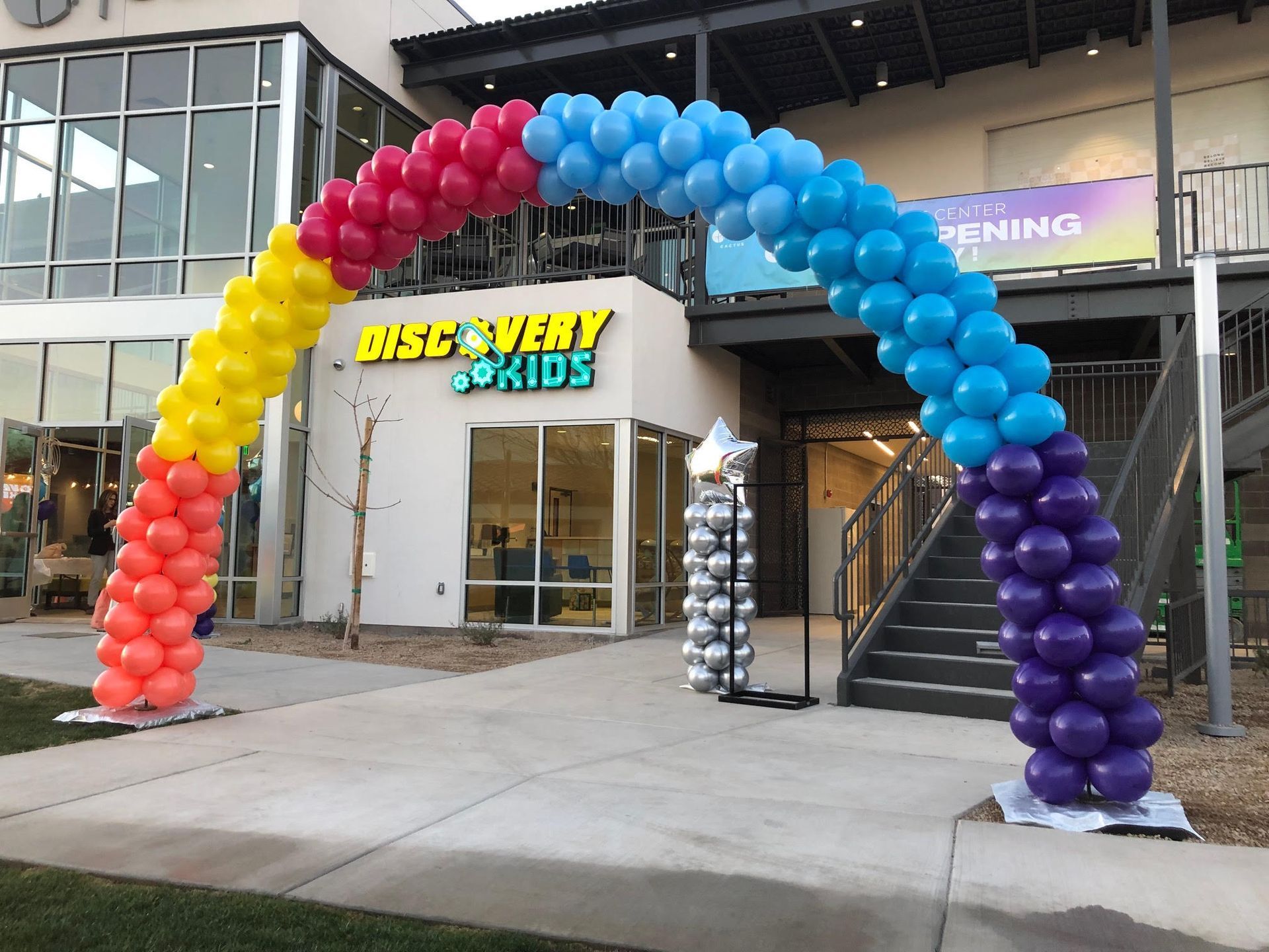A rainbow colored balloon arch in front of a building that says discovery kids