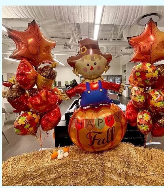 A balloon scarecrow is sitting on top of a pumpkin that says happy fall