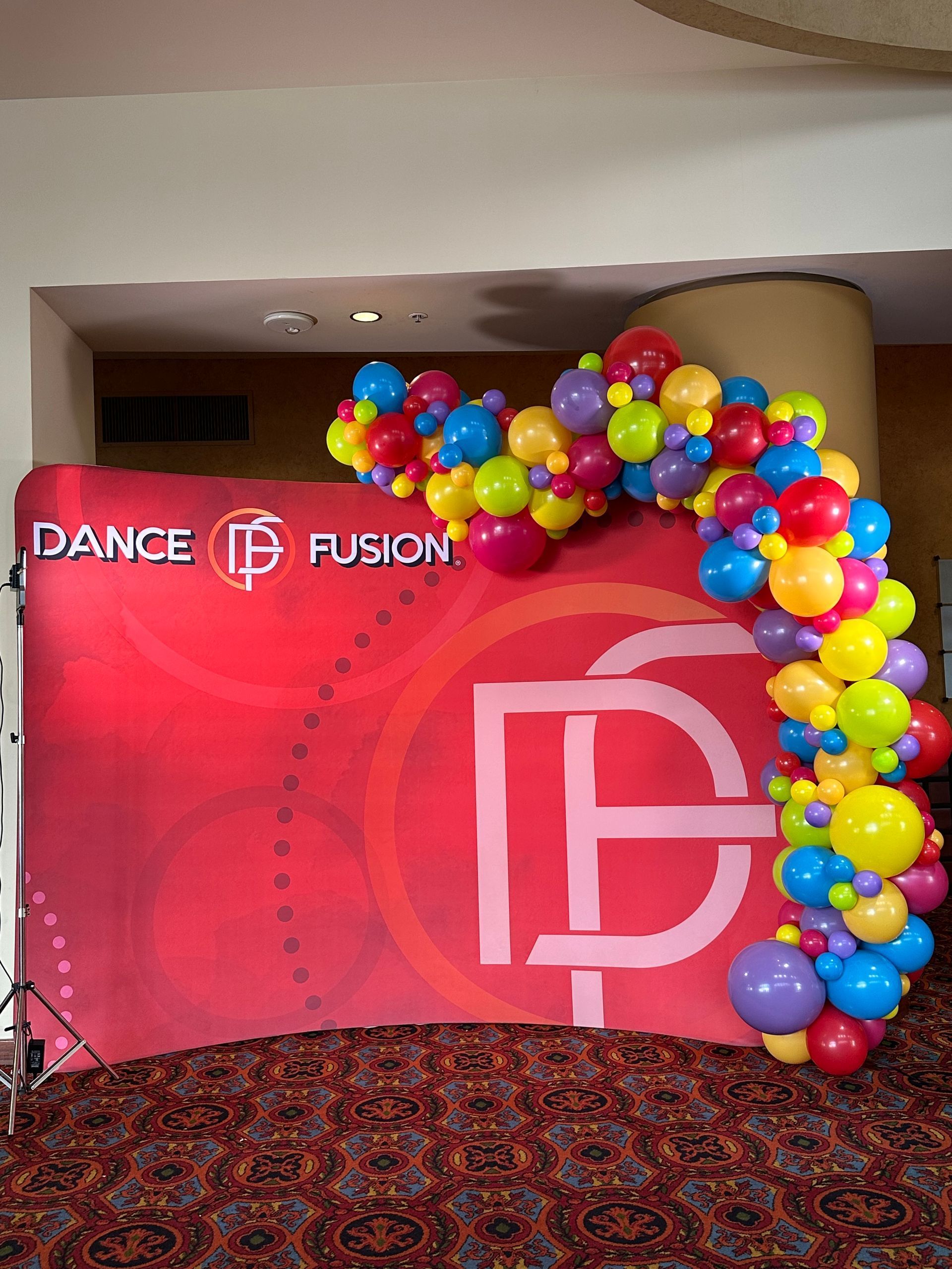 A colorful balloon arch in front of a dance fusion banner
