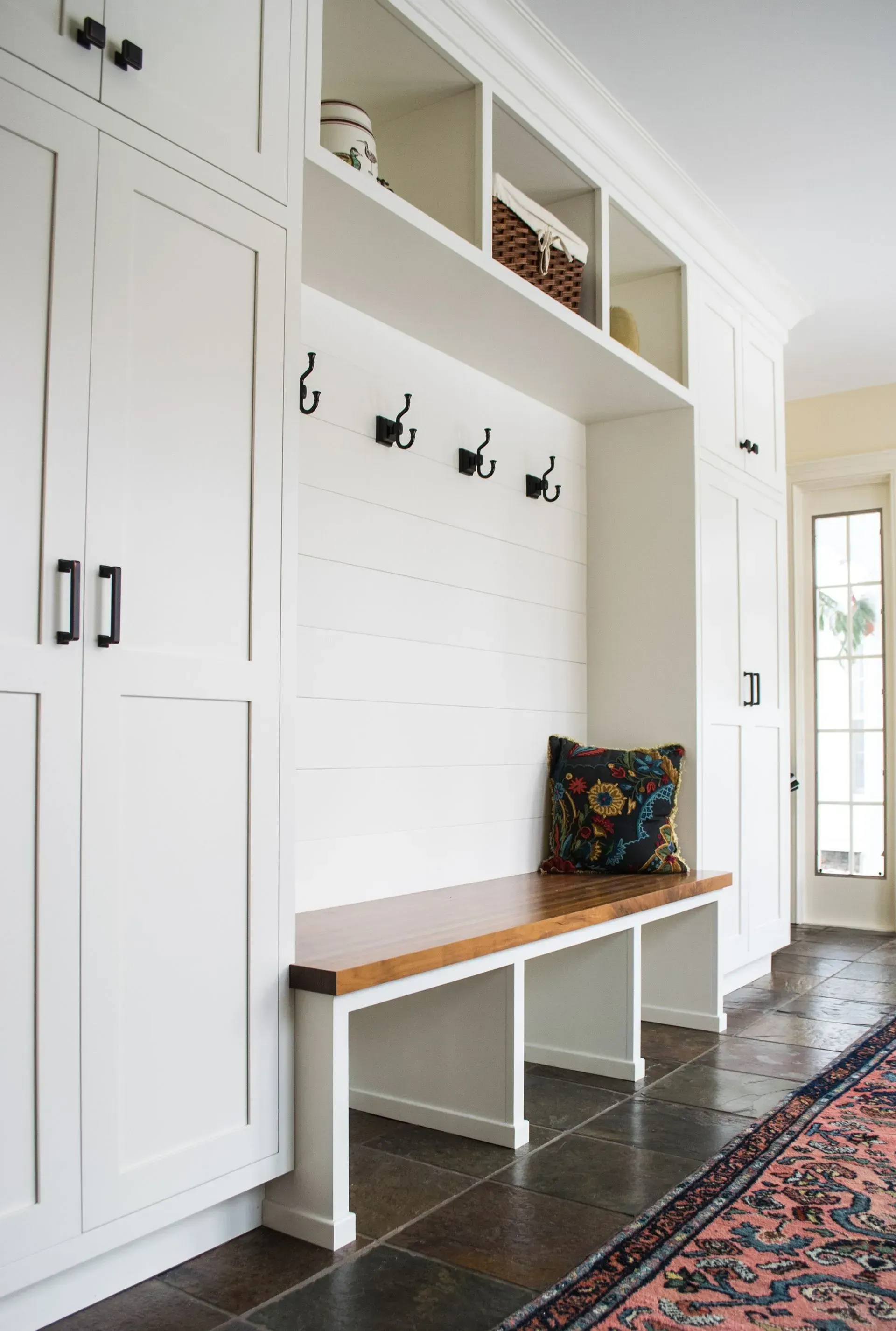 A hallway with white cabinets and a wooden bench.