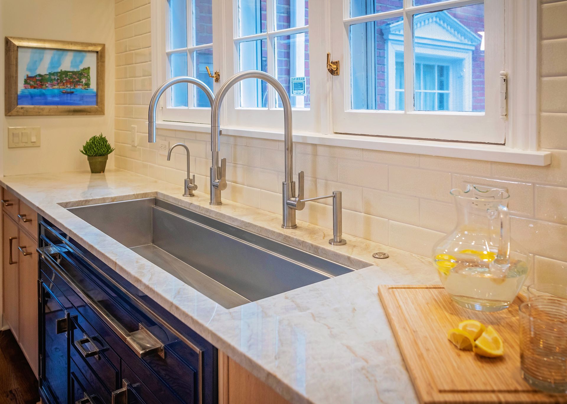 A kitchen sink with two faucets and a pitcher of lemonade on the counter.