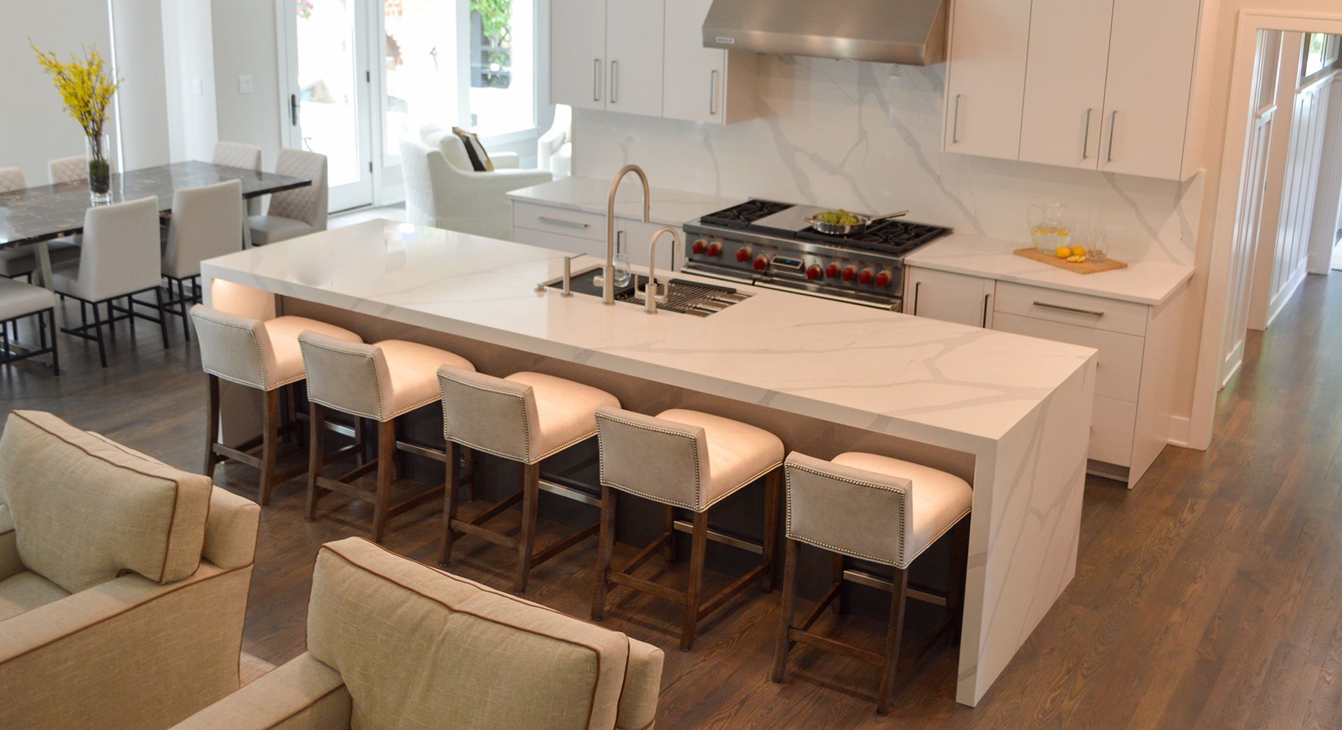 A kitchen with a large island and stools in a living room.
