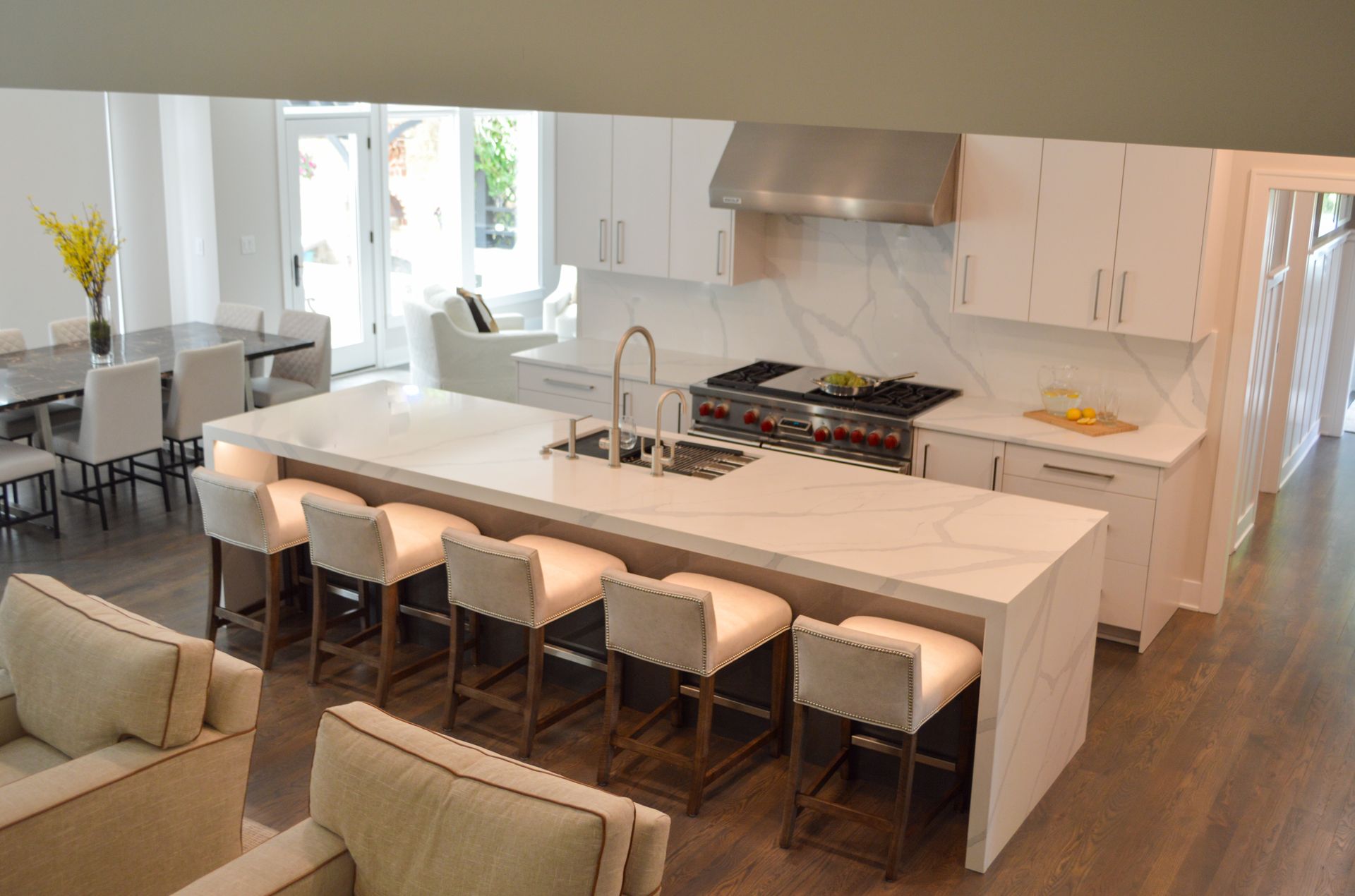 A kitchen with a large island and stools in a living room.