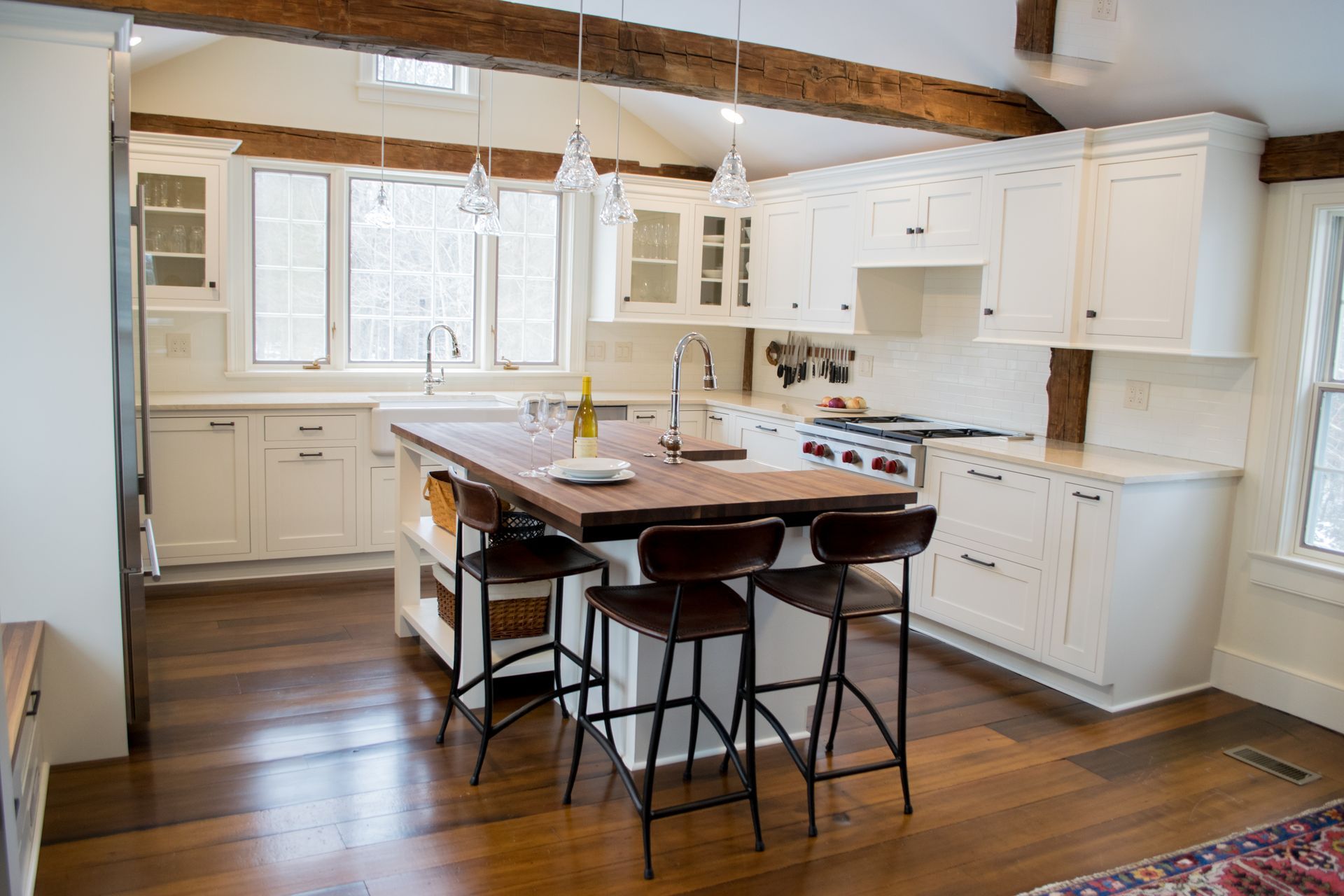 A kitchen with white cabinets , wooden floors , a large island and stools.