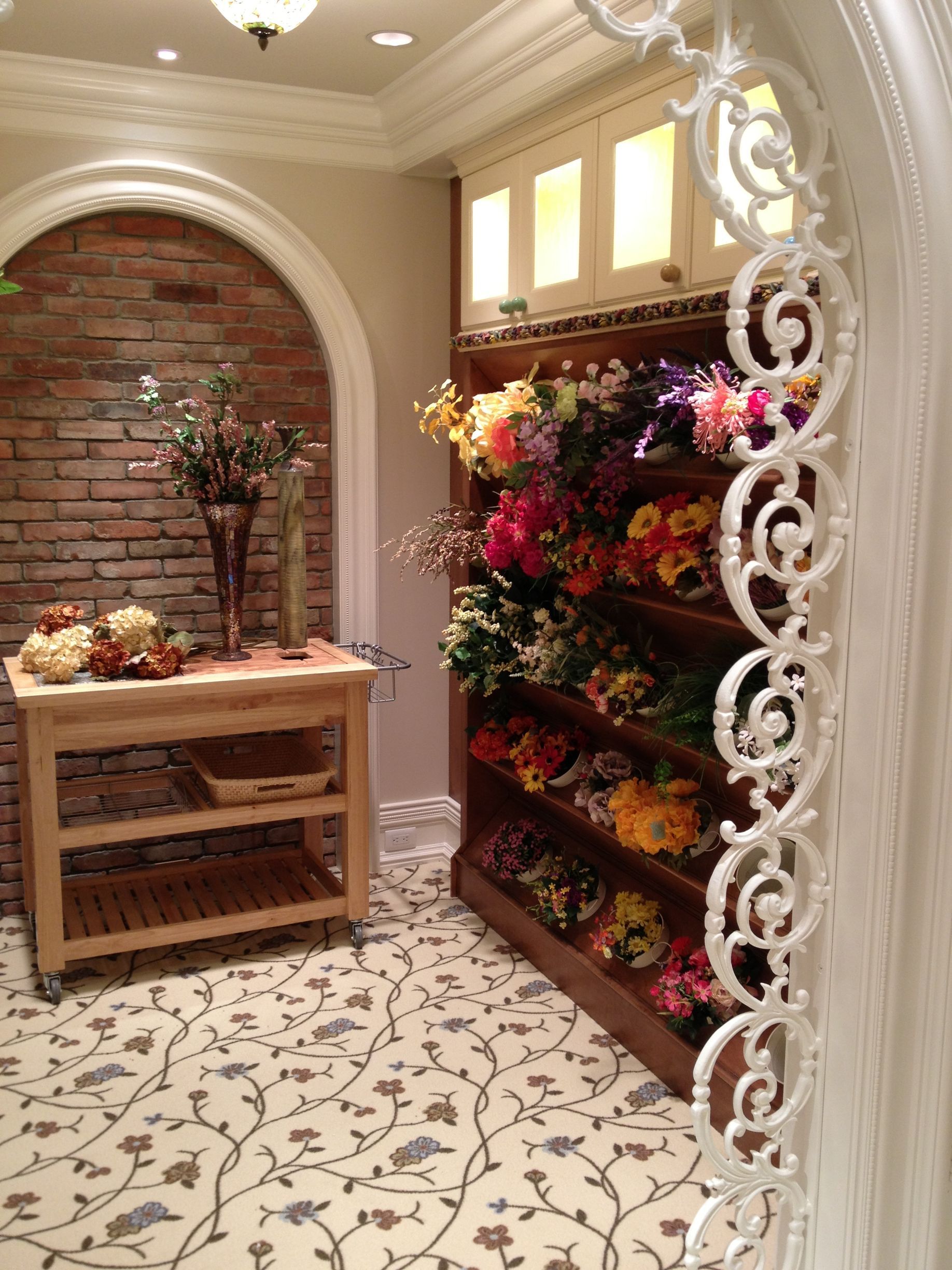 A room with a shelf full of flowers and a table