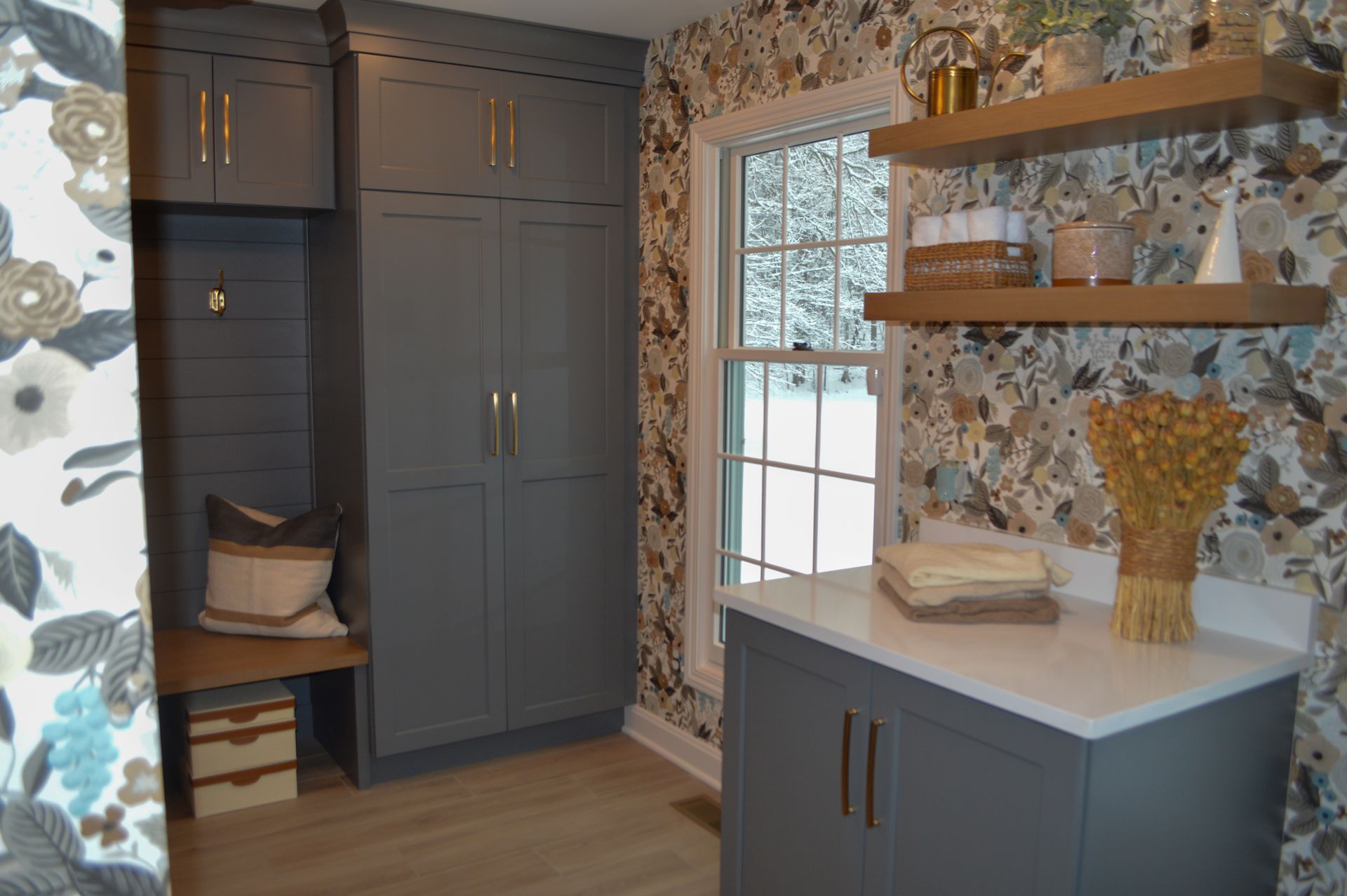 A laundry room with a window , cabinets , shelves and a bench.