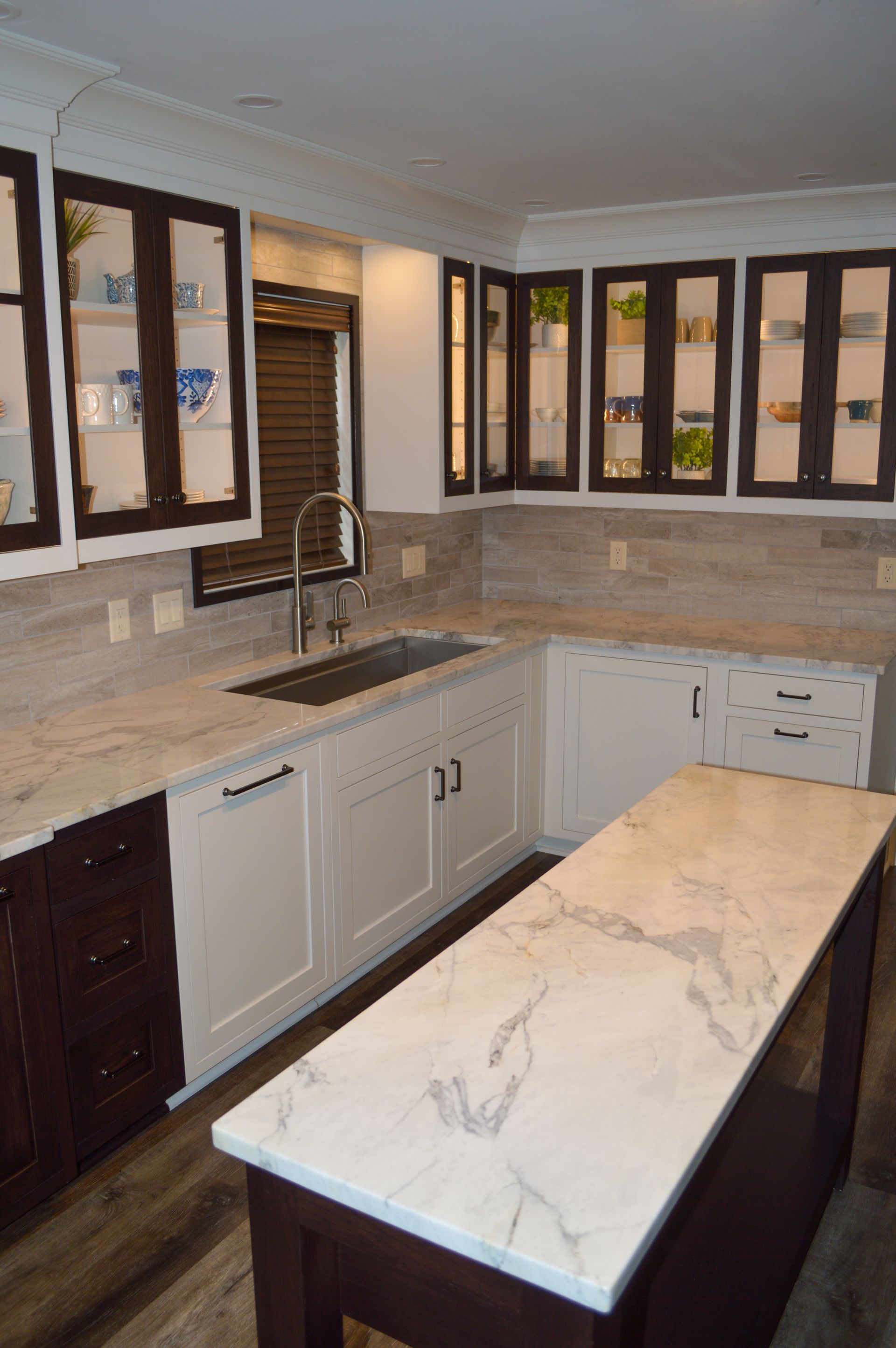 A kitchen with white cabinets , marble counter tops , a sink , and a large island.