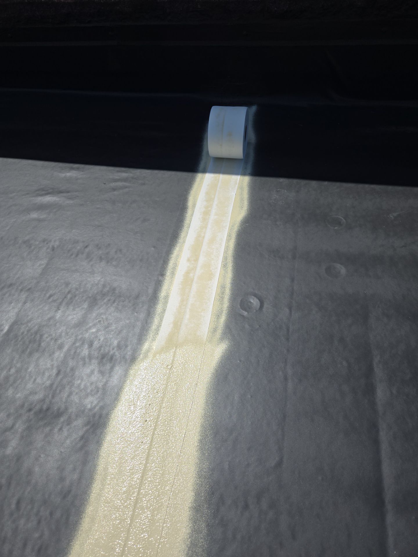 White coating applied to a dark surface with a roller, creating a bright stripe against a dark background.