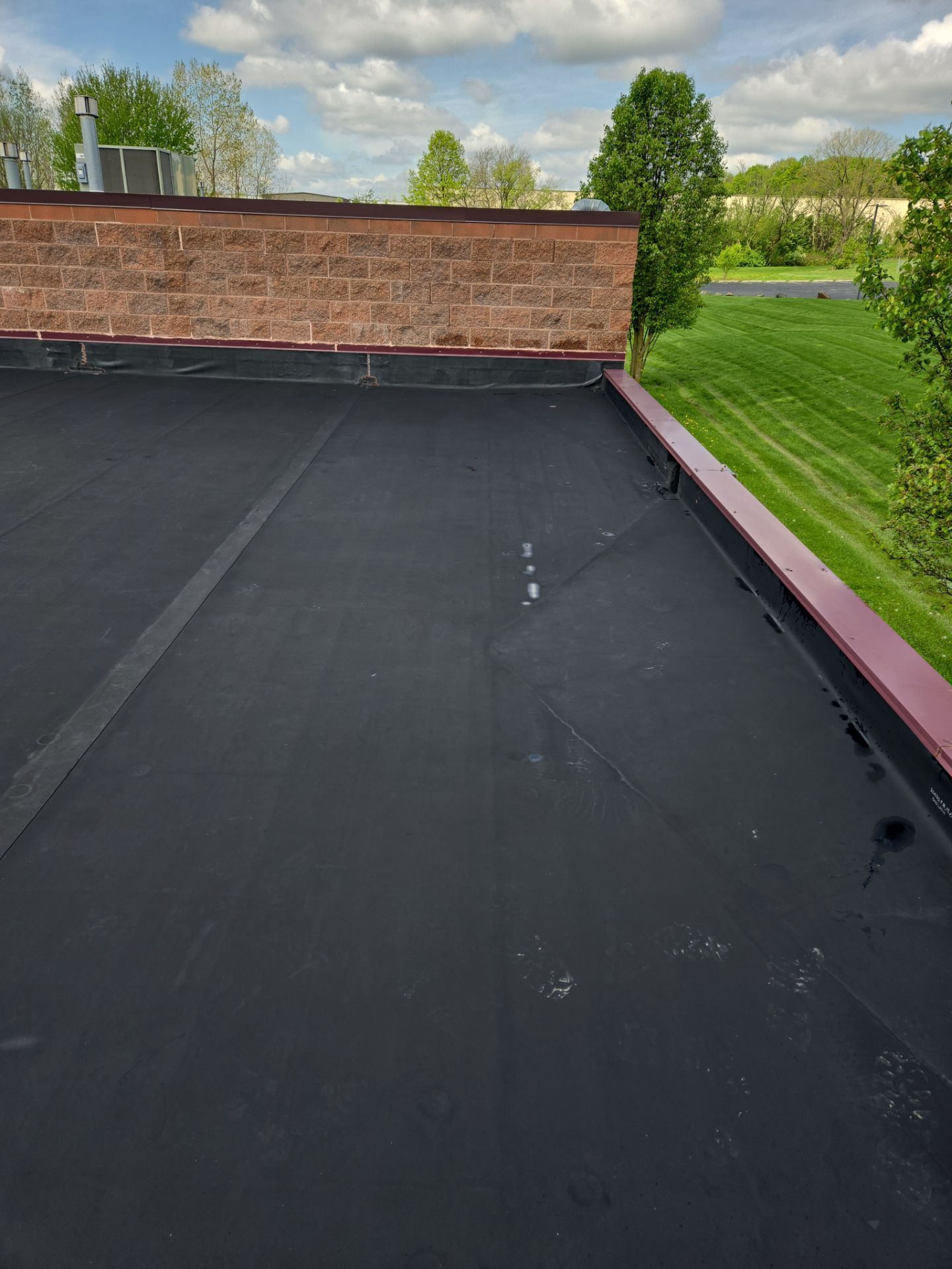 Flat black roof with red trim, brick wall, and green grass in the background. Blue sky with clouds.