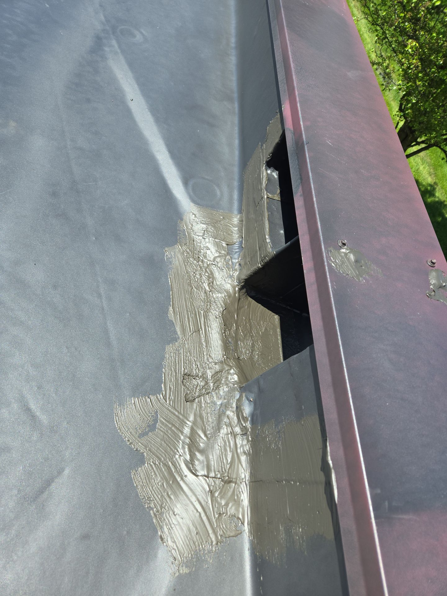 Black roof gutter with sealant applied near a downspout opening.