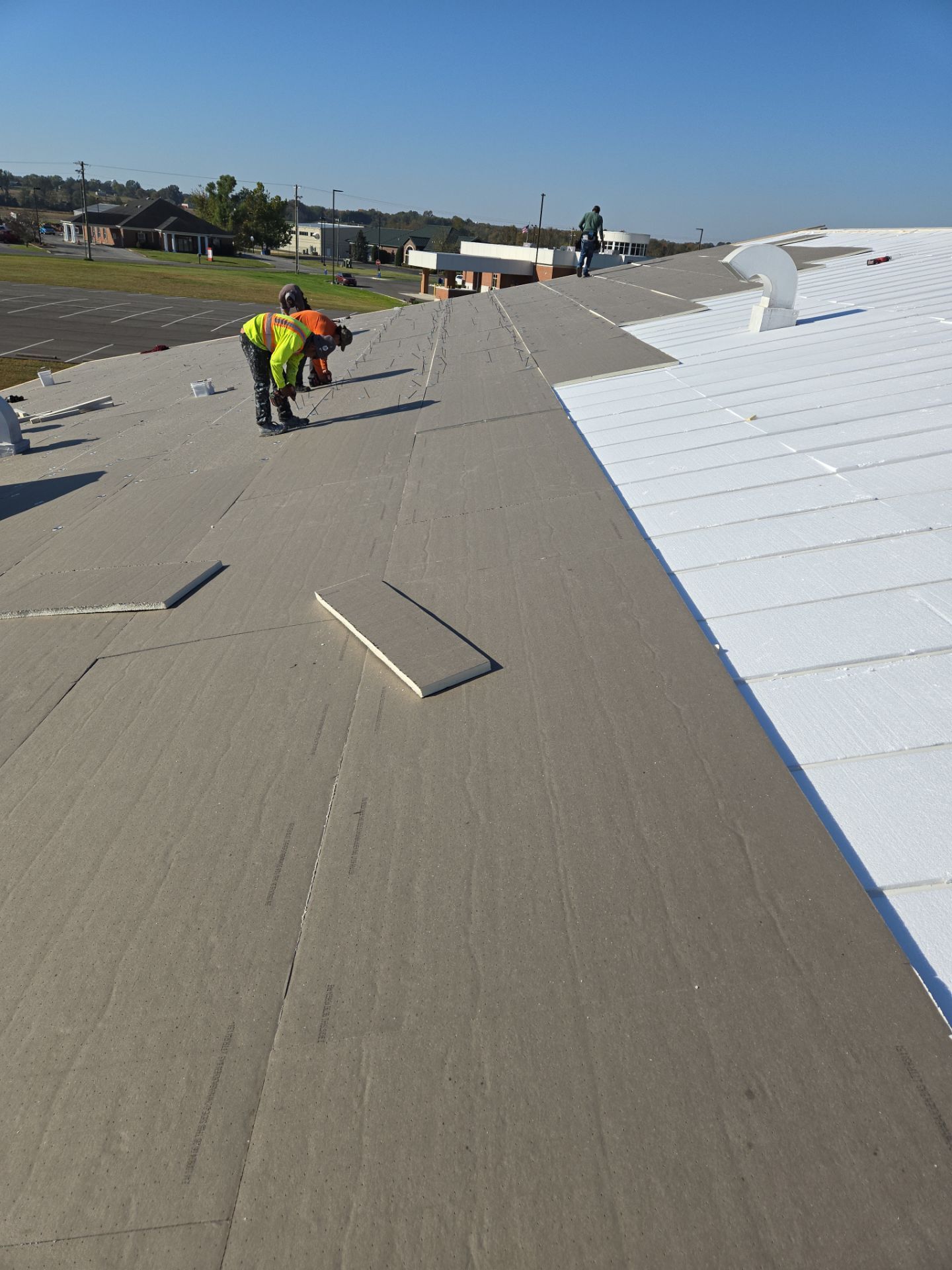 Roofers working on a commercial building roof, installing grey membrane over white insulation.