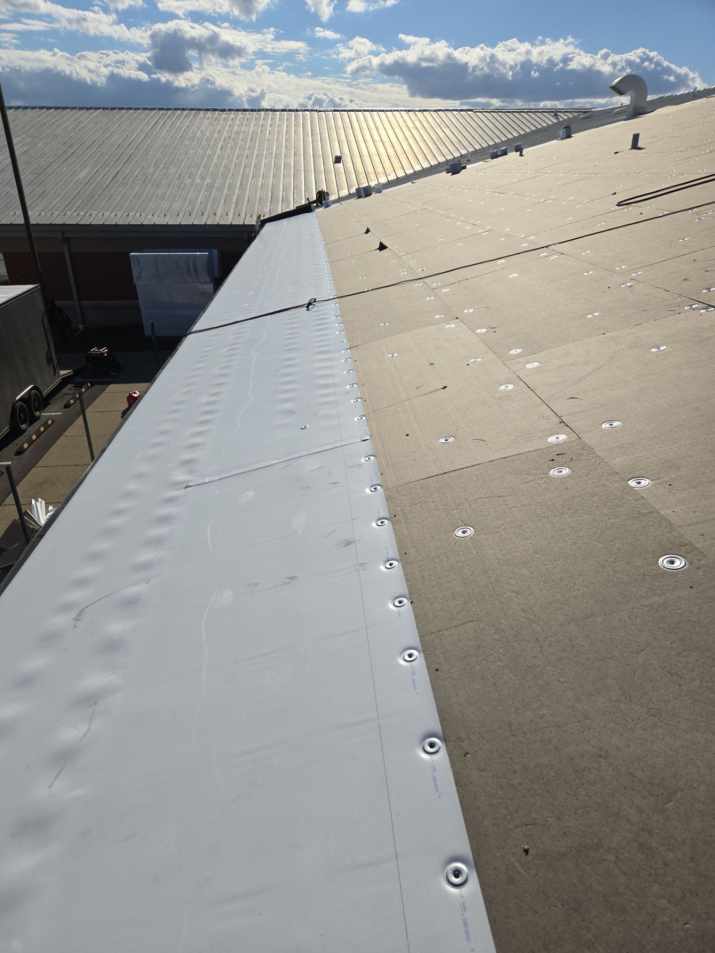 White roofing material being installed on a commercial building, with metal fasteners.