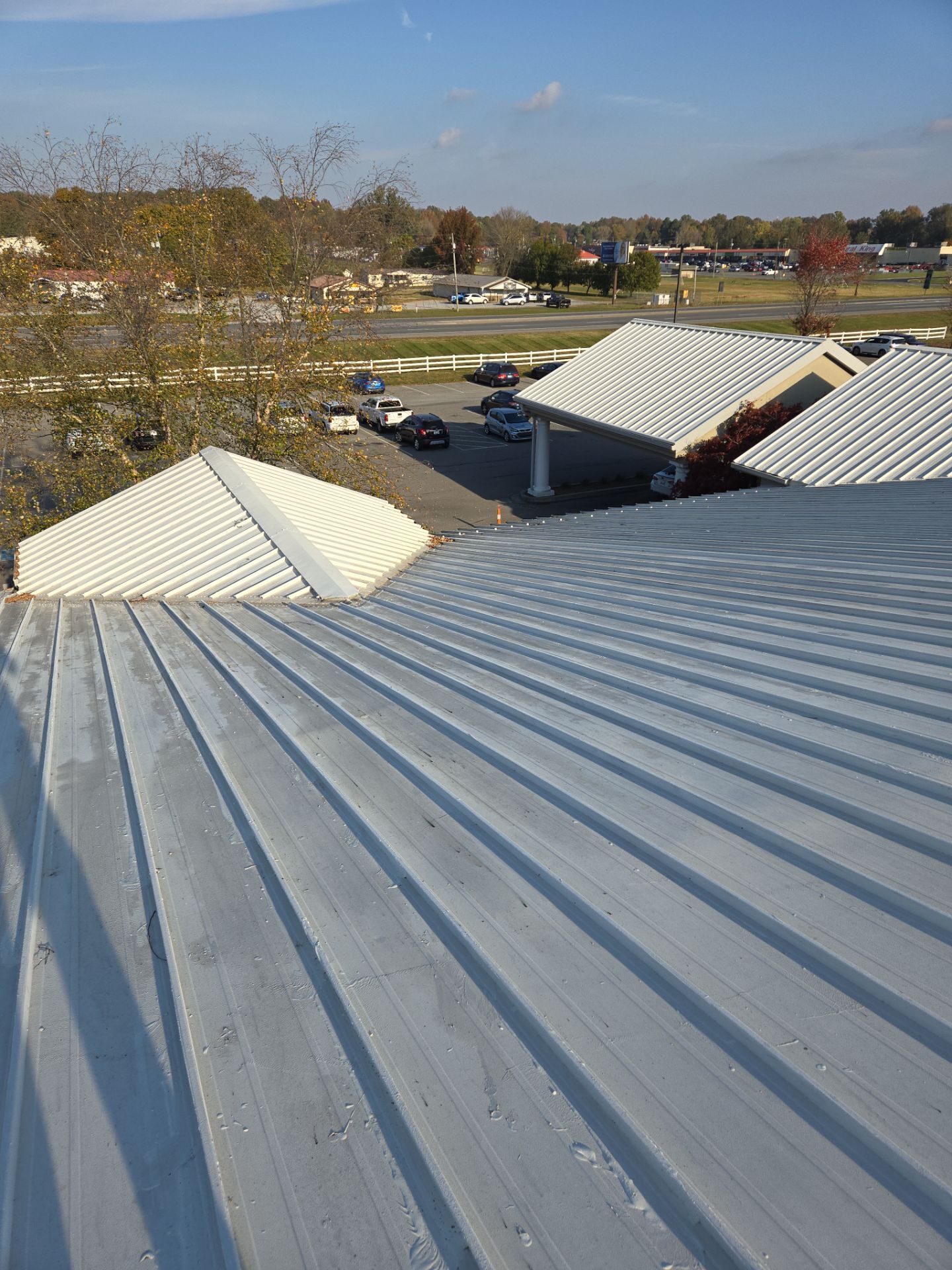 View from a white metal roof, looking toward parking lot and structures. Clear sky.