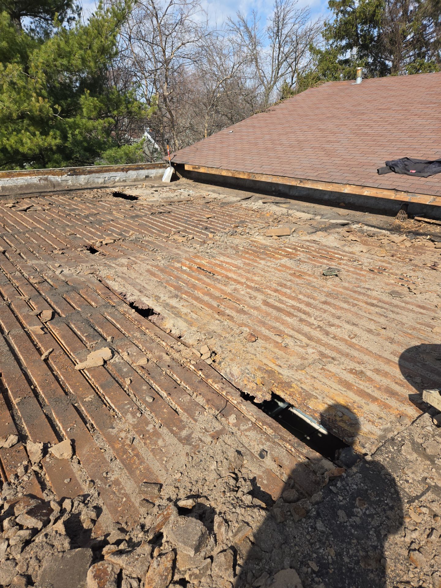 Ripped-up roof deck with exposed boards and debris. Sunlit outdoor setting, partially-shingled roof in background.