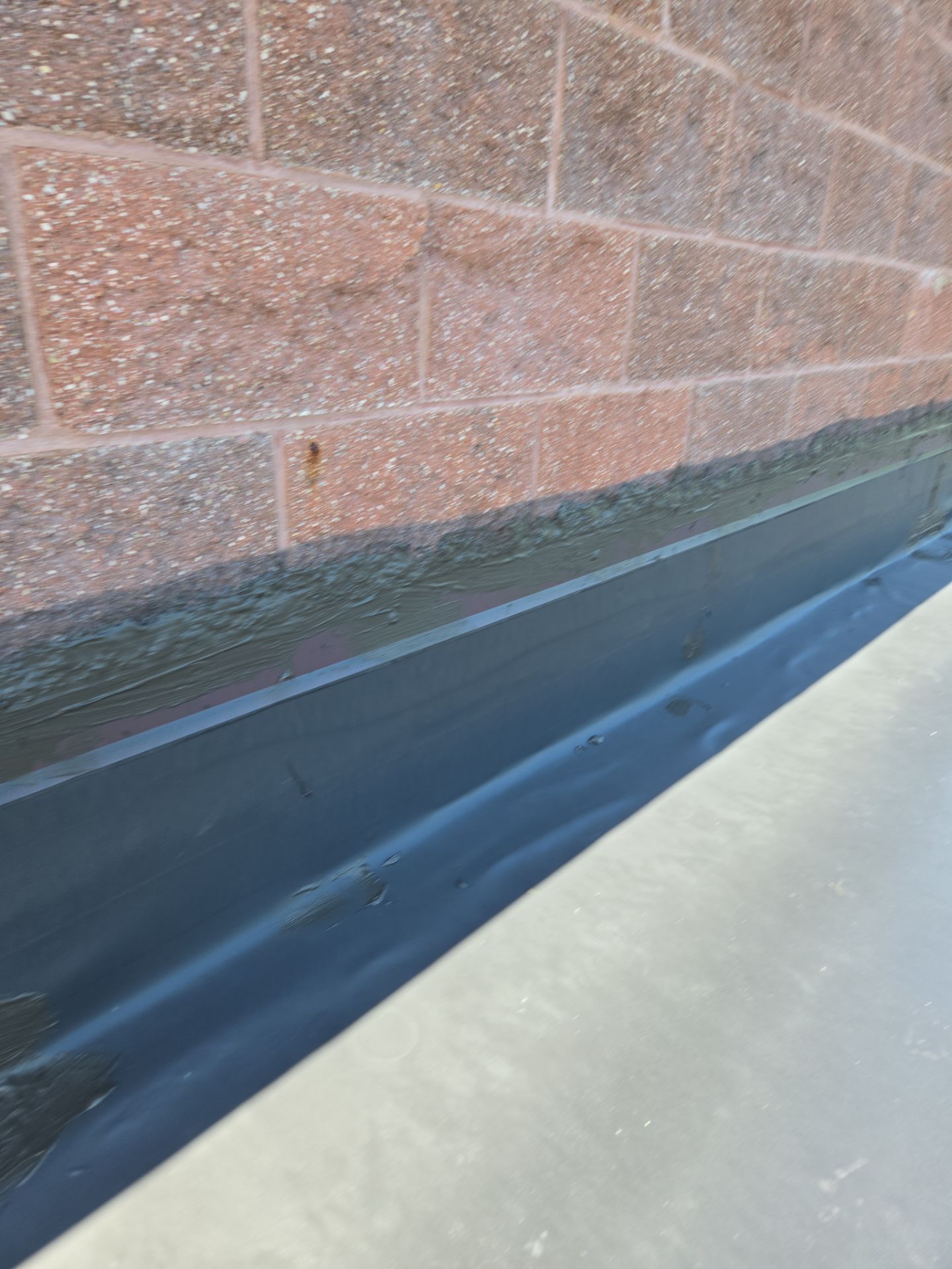 Black roofing material against a red brick wall, with a gray metal edge.