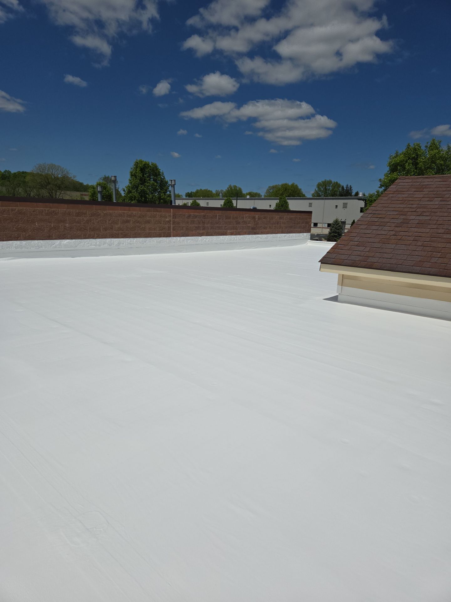 White commercial roof under a bright blue sky with scattered clouds, brick wall backdrop.