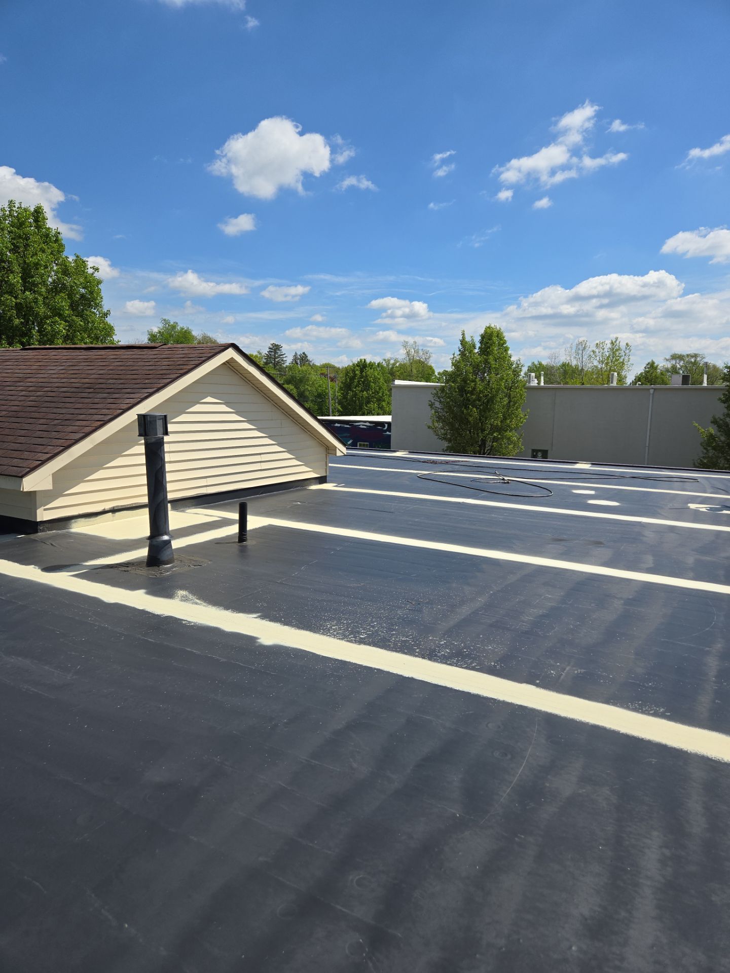 Black flat roof with white lines, a tan roof and blue sky with clouds.