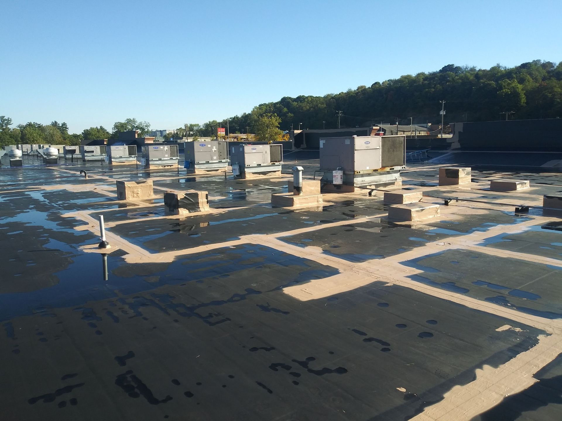 A commercial rooftop with various HVAC units and standing water under a clear sky.