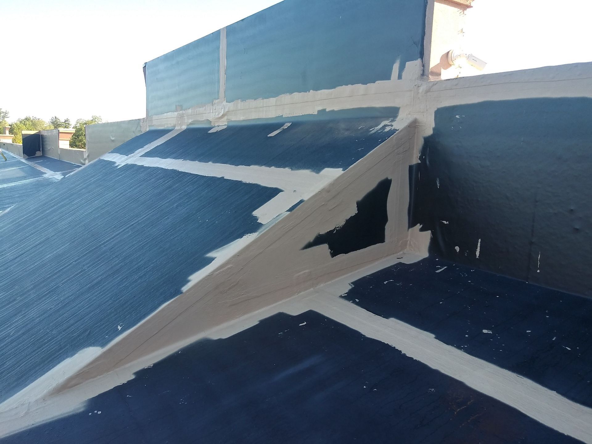 Blue roofing with white sealant around chimney and angled support, in daylight.