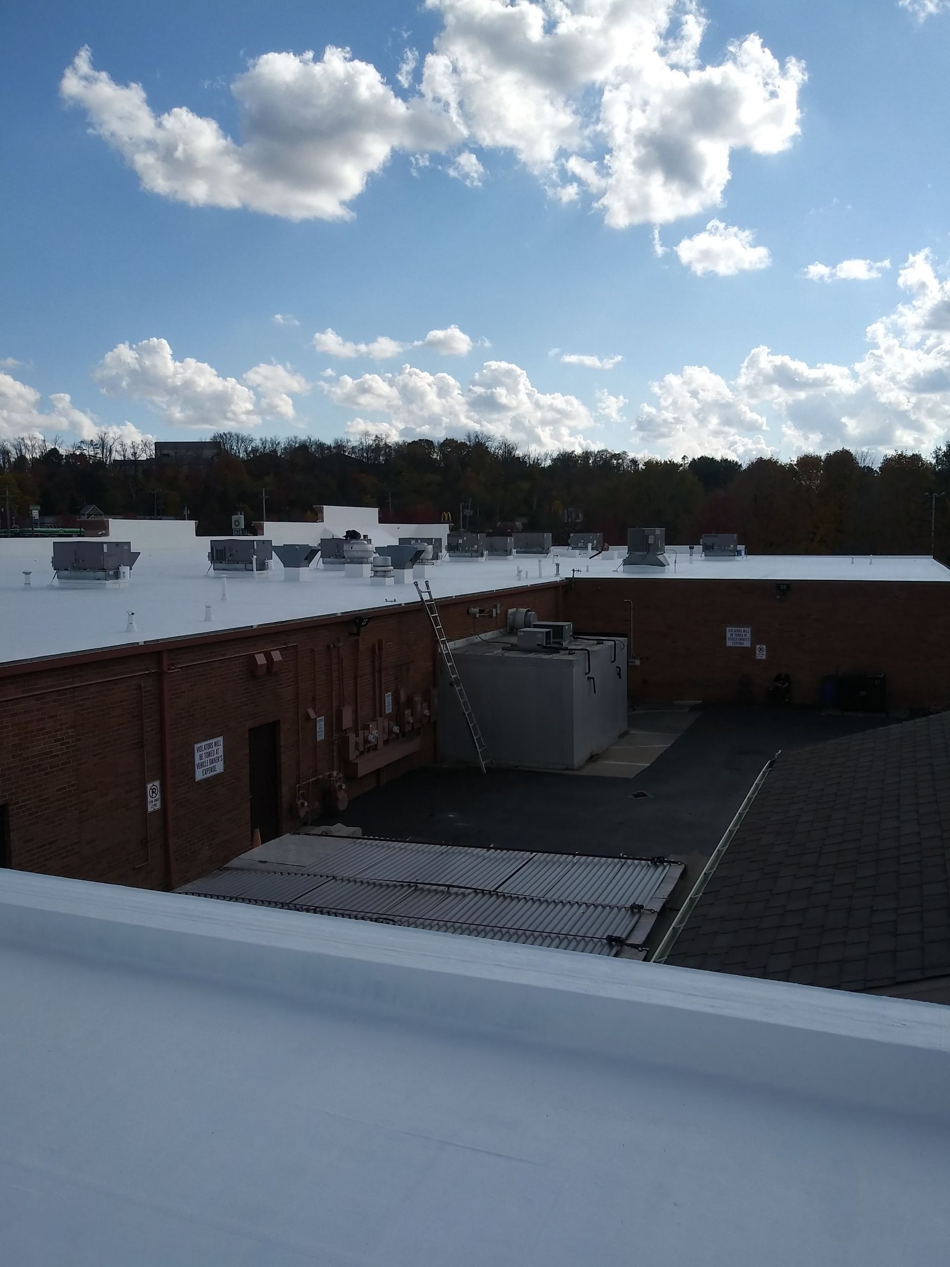 View of a flat white roof, brick building, vents, and a clear blue sky with clouds.