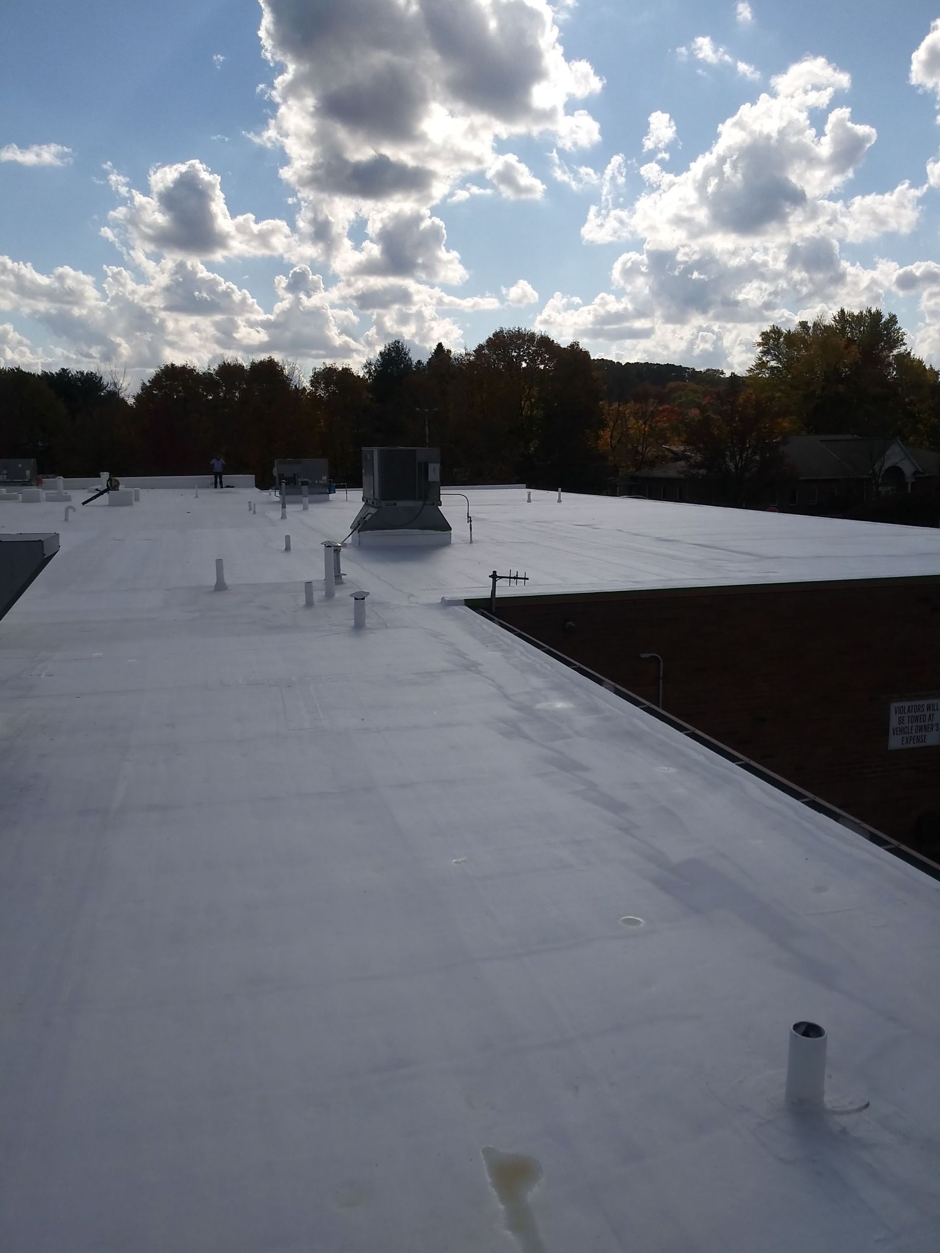 Flat white roof under a partly cloudy blue sky; trees in the background.