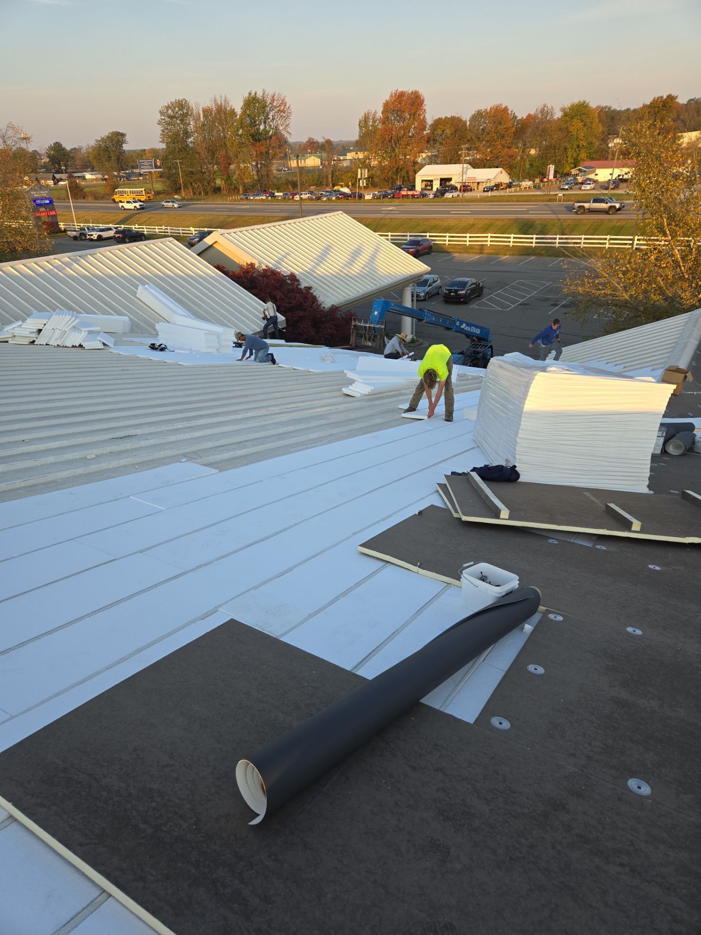 Roofing crew working on a commercial building roof, laying down white and black roofing materials on a sunny day.