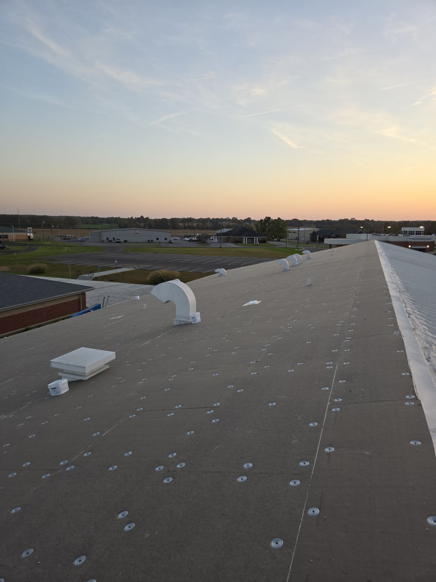 A flat roof with vents, during a sunset, with a distant view of buildings and land.