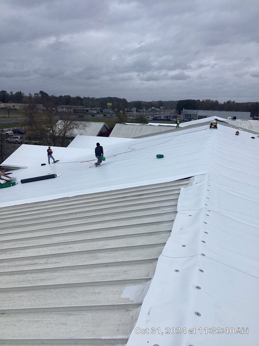 Roofers working on a white commercial roof under a cloudy sky.