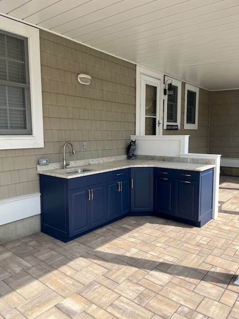 A kitchen with blue cabinets and a sink on a patio under the deck