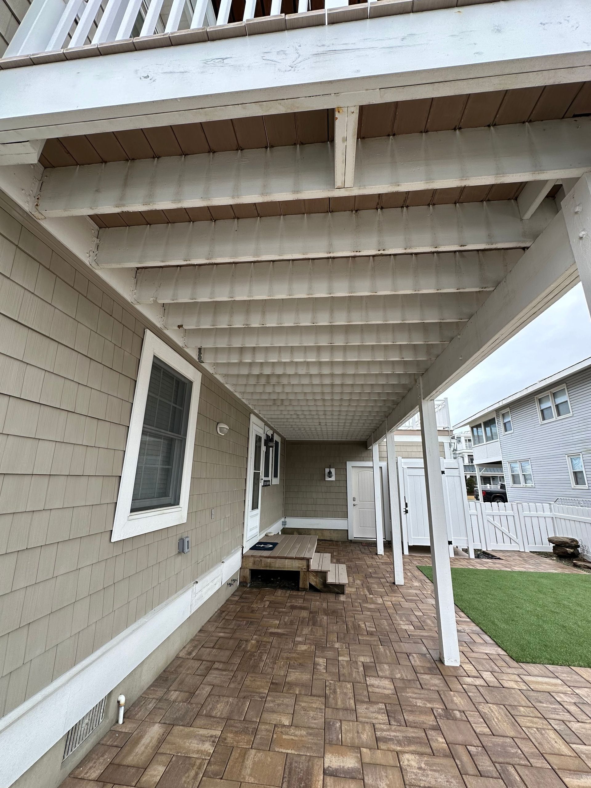 A covered walkway leading to a house with a balcony under deck before renovation