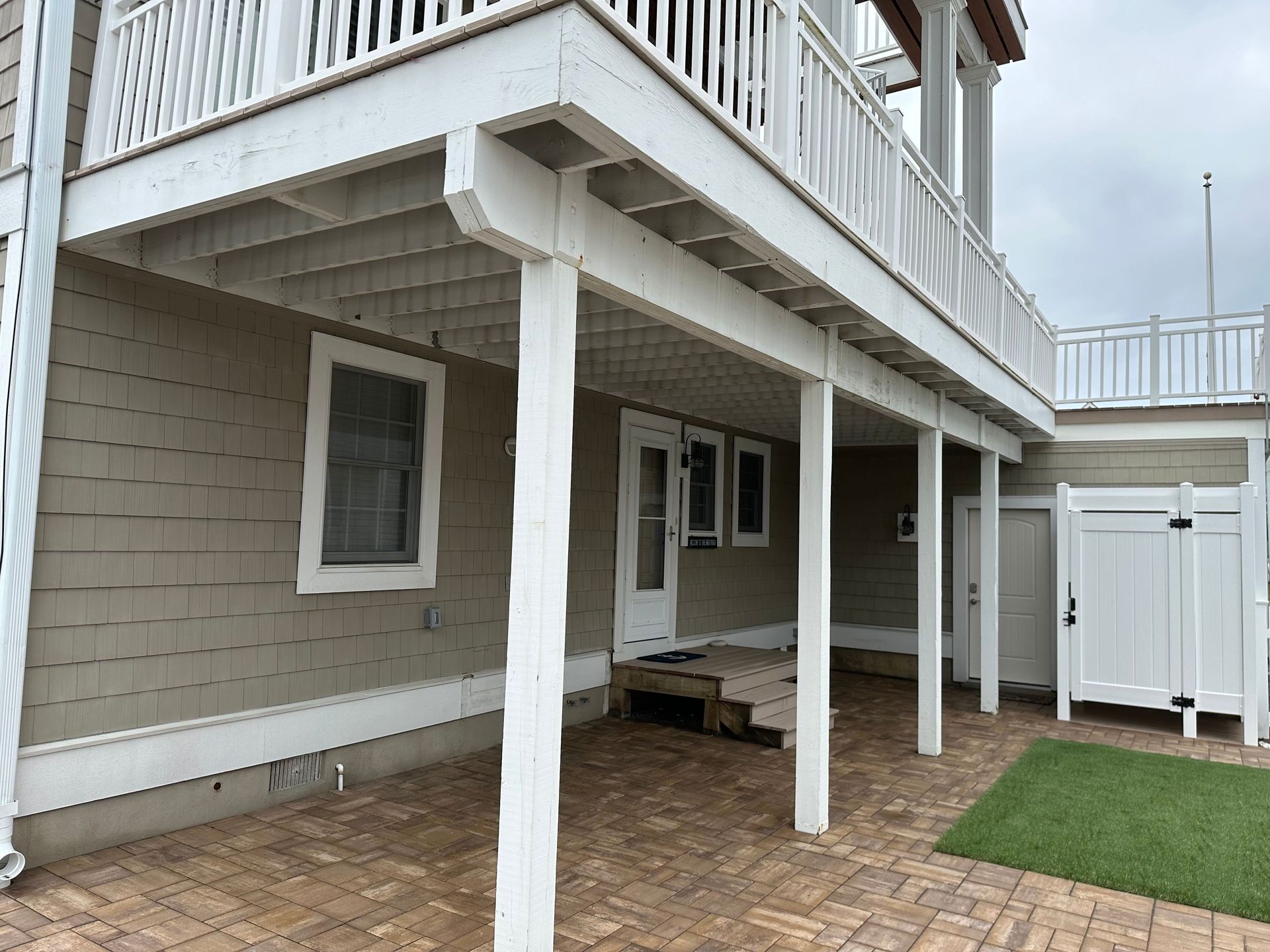 The back of a house with a white deck and a white railing before under deck renovation