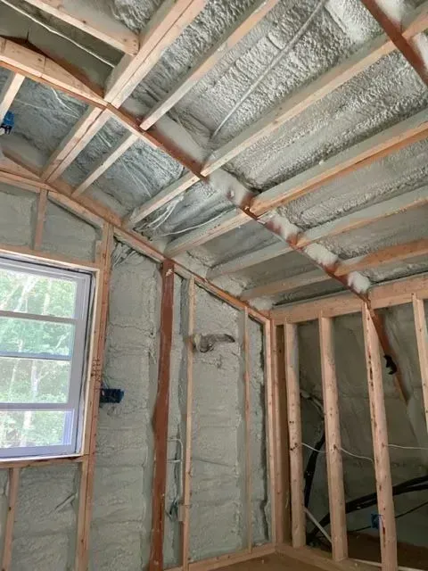 Interior of a building under construction, insulated with spray foam. Wooden frame with a window visible.