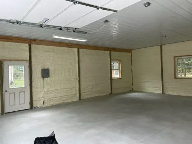 Interior view of a garage with spray foam insulation on the walls and a concrete floor.