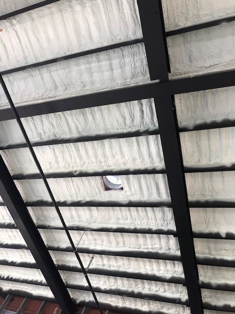 View of a ceiling with dark beams and white insulation, showing a ventilation fixture.