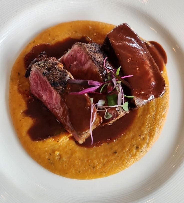 A white plate topped with meat and sauce on a table