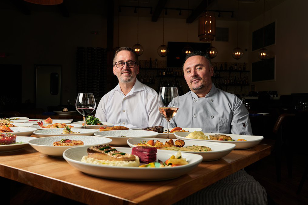 Two men are sitting at a table with plates of food and wine glasses.
