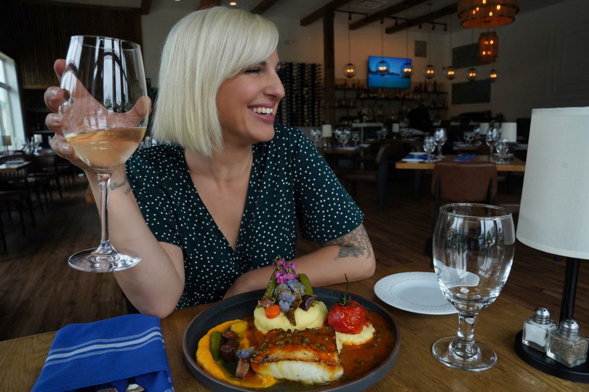A woman is sitting at a table with a plate of food and a glass of wine.