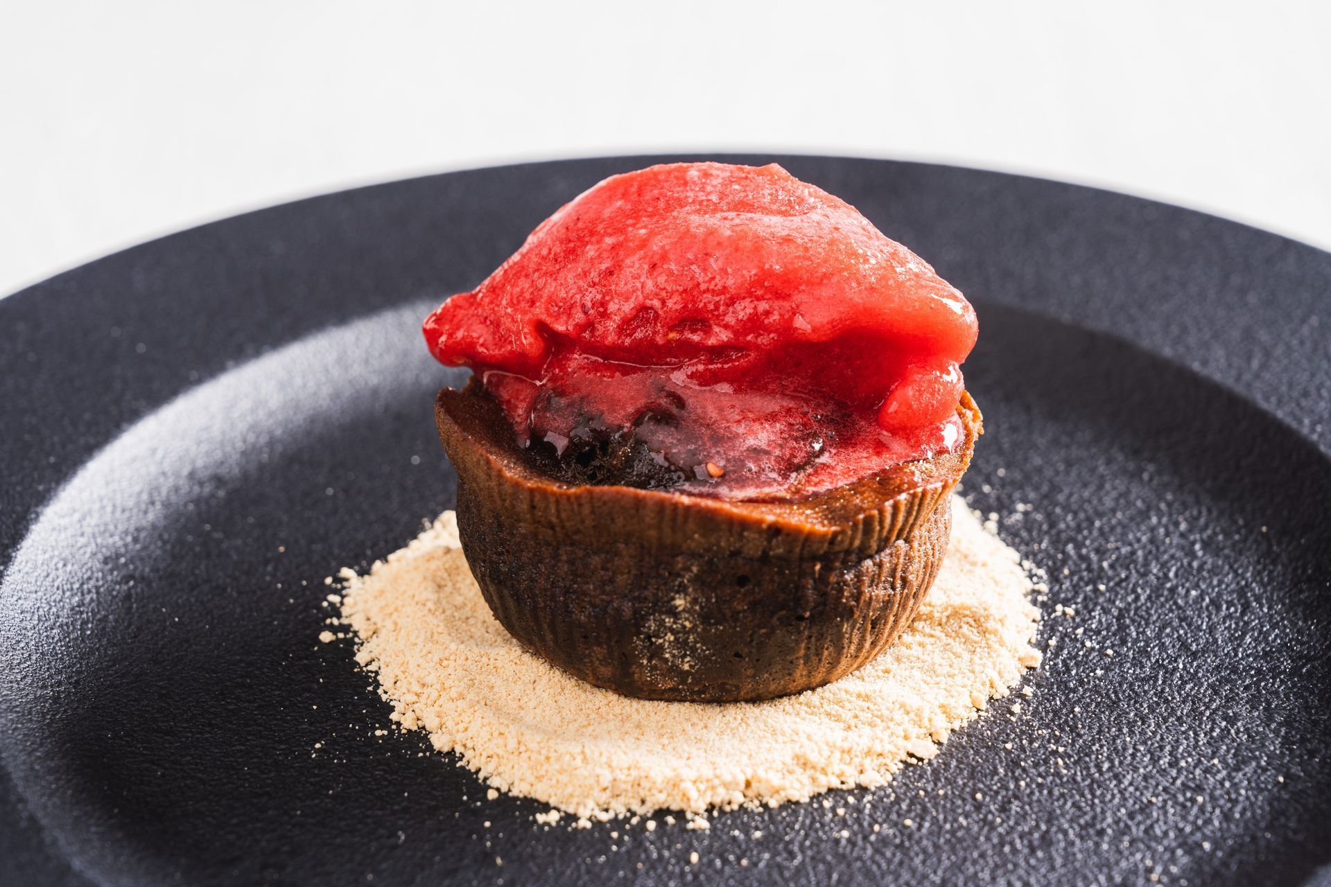 Chocolate cake with red sorbet on a bed of crumbs, served on a black plate