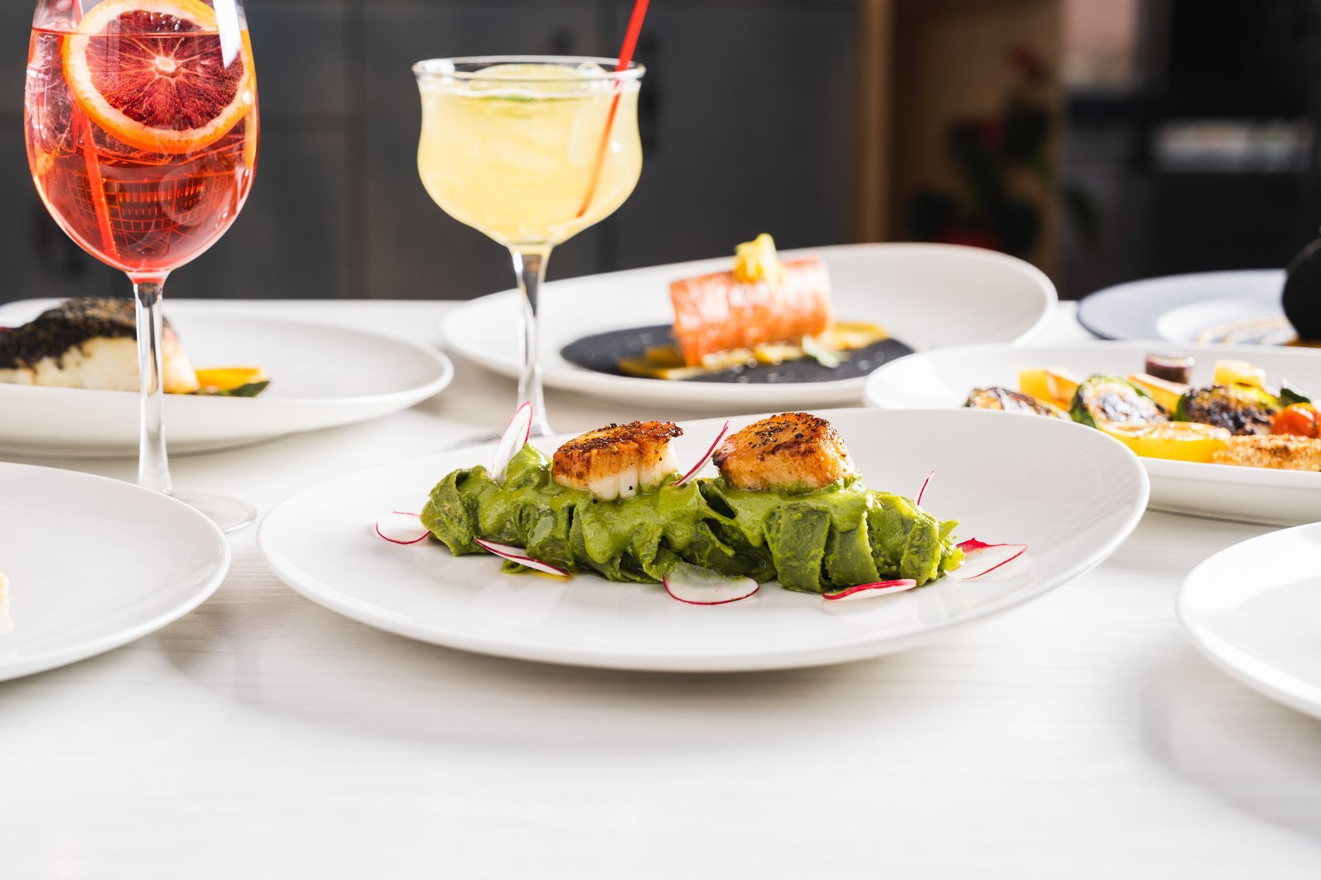 Table with various dishes, cocktails: Seafood appetizer, salad, pasta, salmon, and drinks