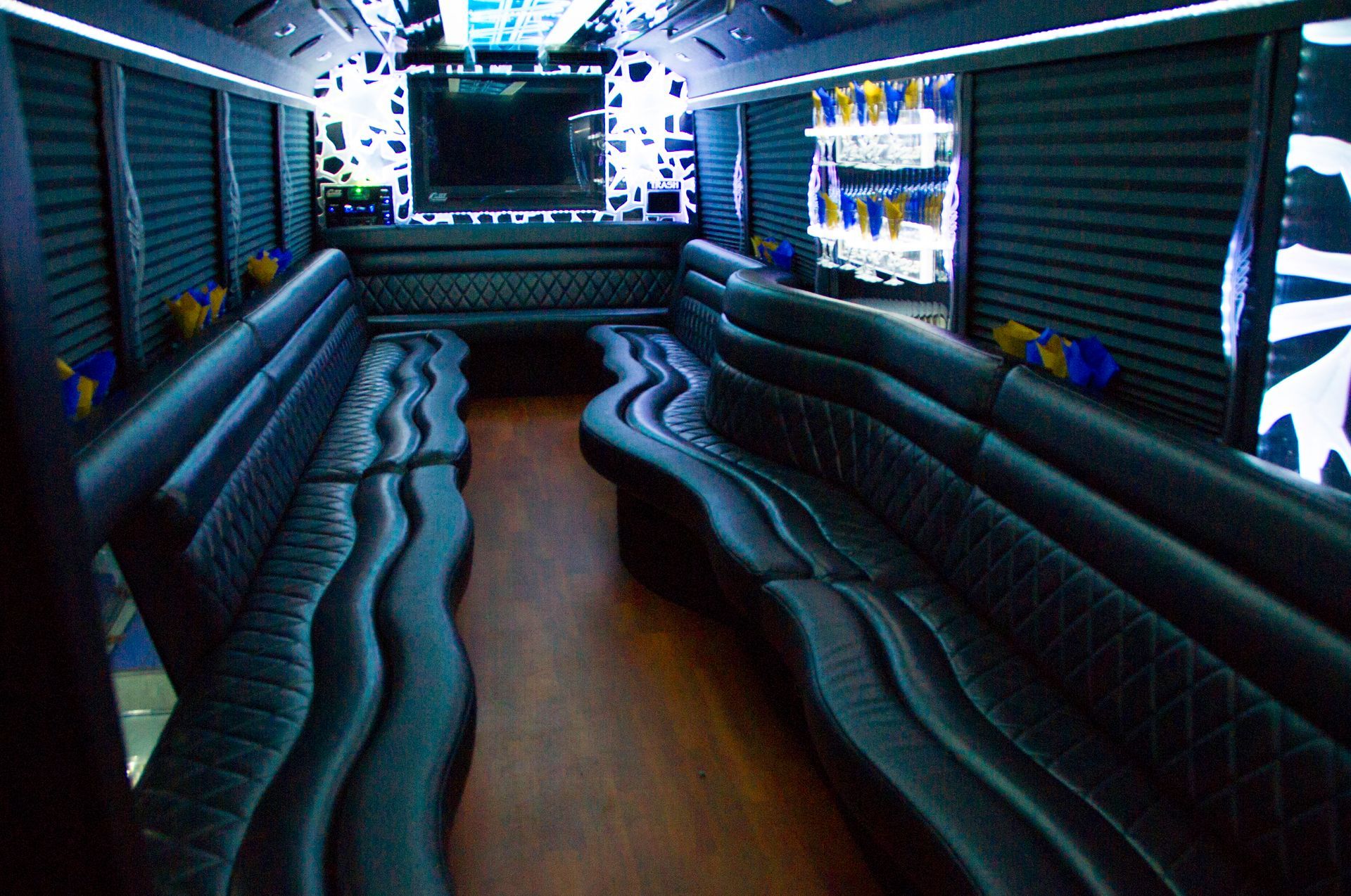 Long, wavy seats inside a dark blue lounge or bus interior with a wooden aisle and TV screens at the front